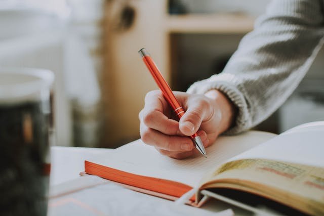 Close-up of a person's hand writing in a journal with prompts related to self-discovery